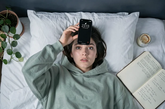 Jeune femme allongée regardant l'heure 23h13 sur son téléphone la nuit, évoquant la signification spirituelle et numérologique des heures miroirs